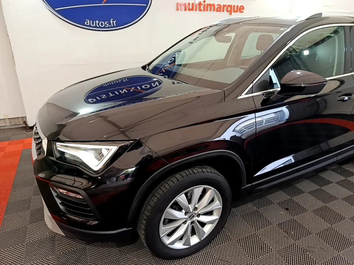 Vue 3/4 avant côté gauche d'un SEAT Ateca noir brillant avec jantes alliage et phares LED allumés en intérieur showroom.