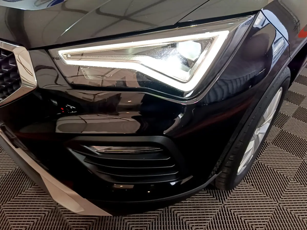 Gros plan sur le phare avant gauche allumé du SEAT Ateca noir, mettant en valeur la calandre et la roue avant.