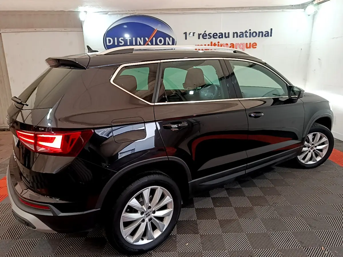Vue 3/4 arrière côté gauche d'un SEAT Ateca noir avec feux arrière allumés et jantes alliage en showroom.