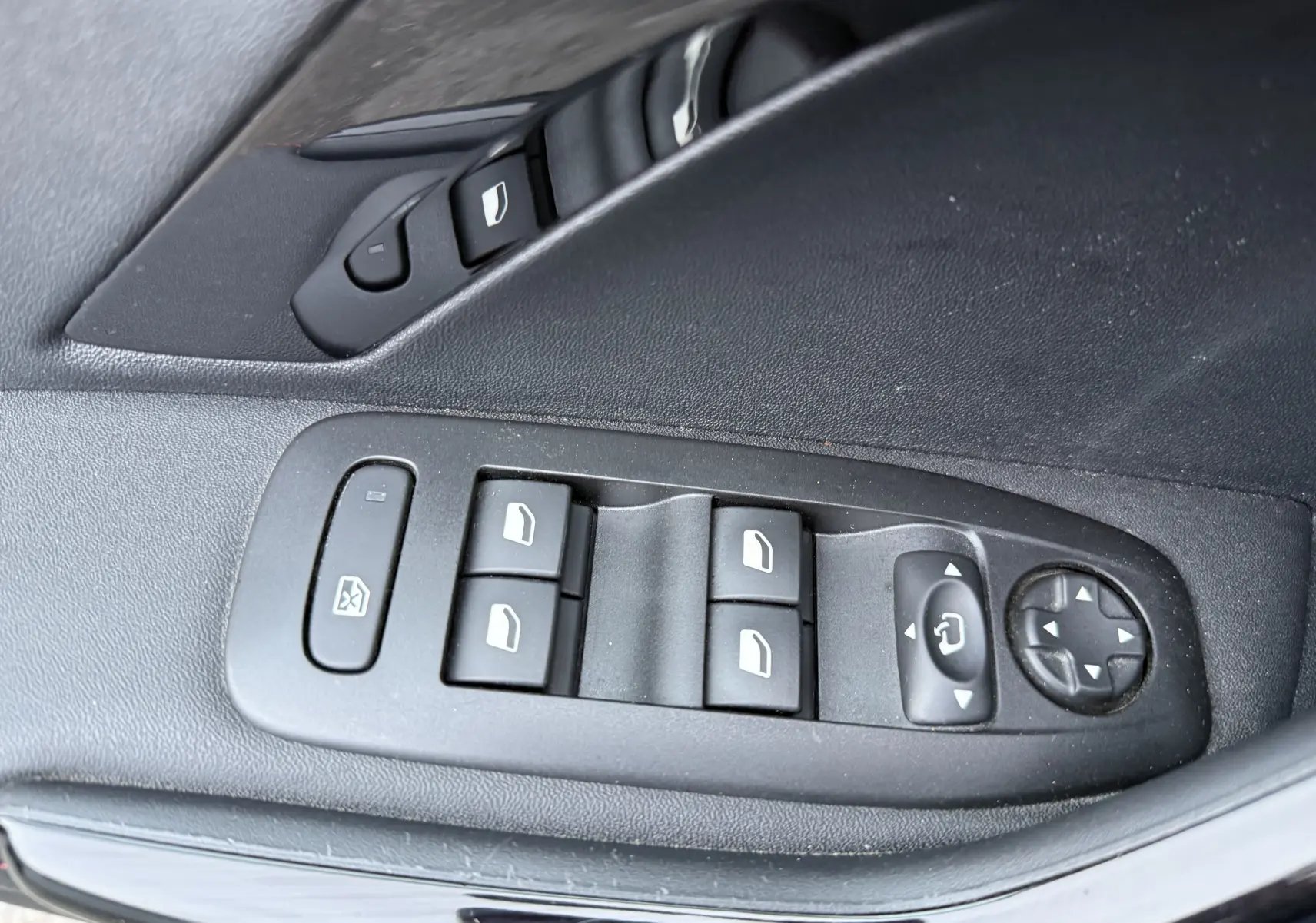 Gros plan sur les commandes de lève-vitres et réglage des rétroviseurs côté conducteur du Peugeot 2008 noir 2018.