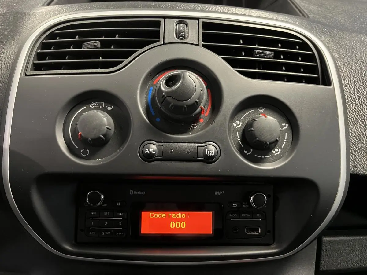 Gros plan sur la console centrale noire du Renault Kangoo Express gris foncé, avec commandes de climatisation et radio affichant "Code radio : 000"