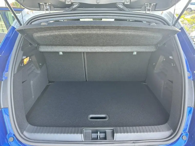 Coffre ouvert vu de l'arrière d'un Renault Captur 2025 bleu Flamme, avec cache-bagages relevé et intérieur noir.