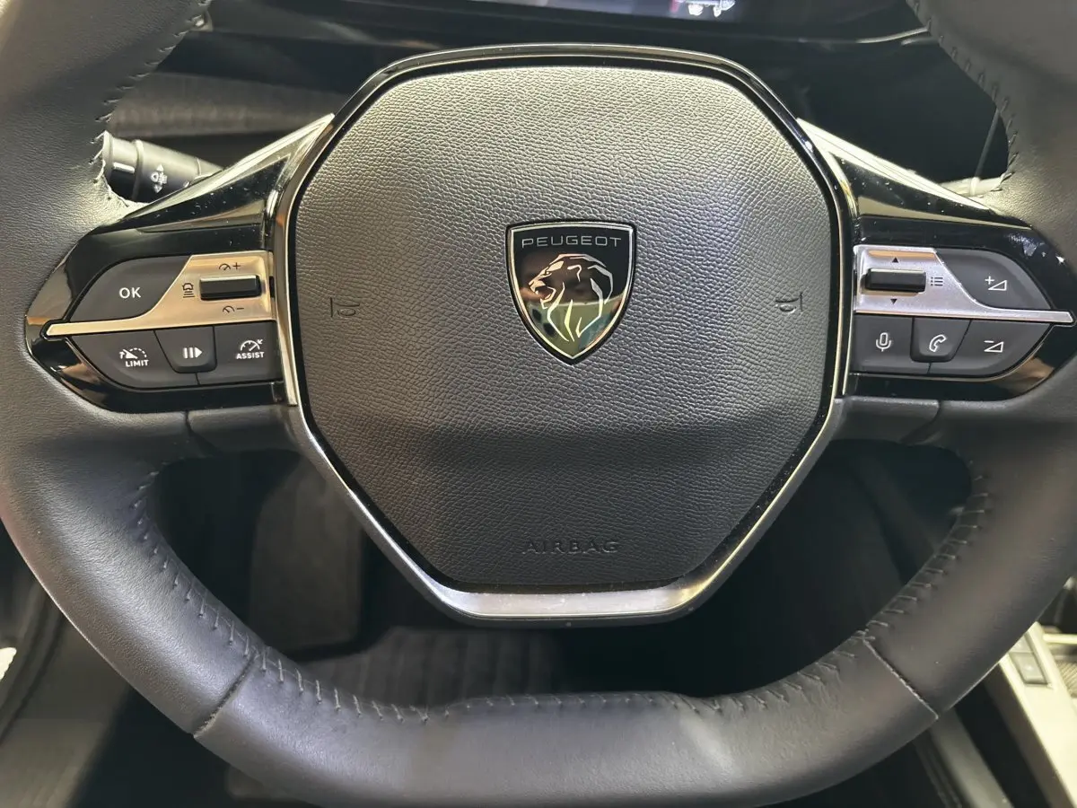 Gros plan sur le volant cuir noir de la Peugeot 308 PureTech 130 S&S Allure 2024 avec commandes multifonctions intégrées.