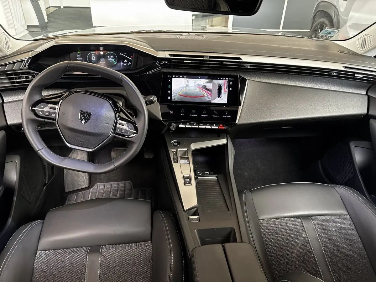 Vue intérieure avant de la Peugeot 308 gris clair, volant cuir, écran tactile affichant la caméra de recul.