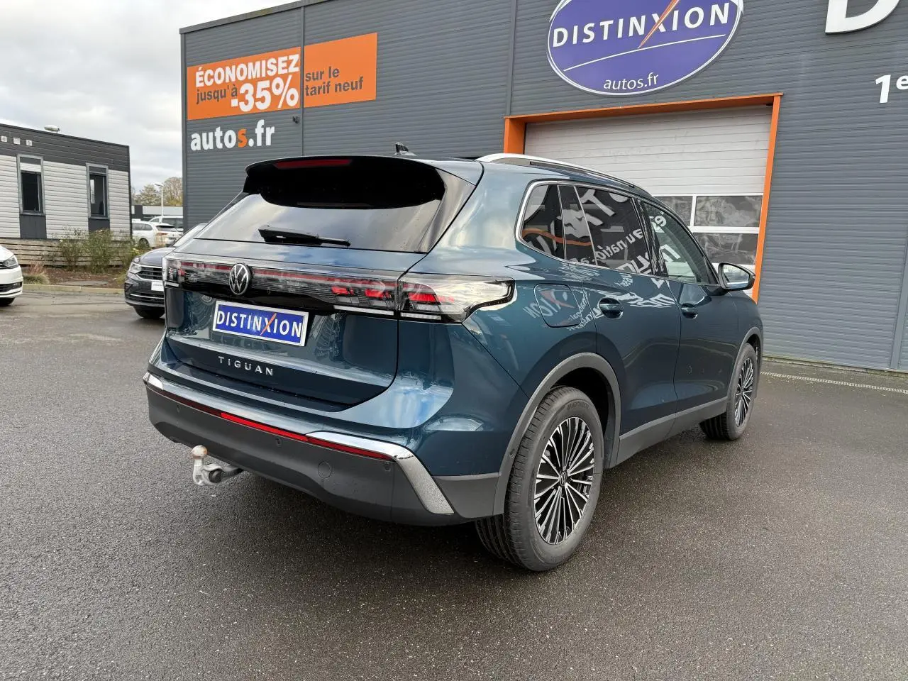Vue 3/4 arrière droite du Volkswagen Tiguan 2024 bleu métallisé avec crochet d'attelage escamotable et jantes alliage.