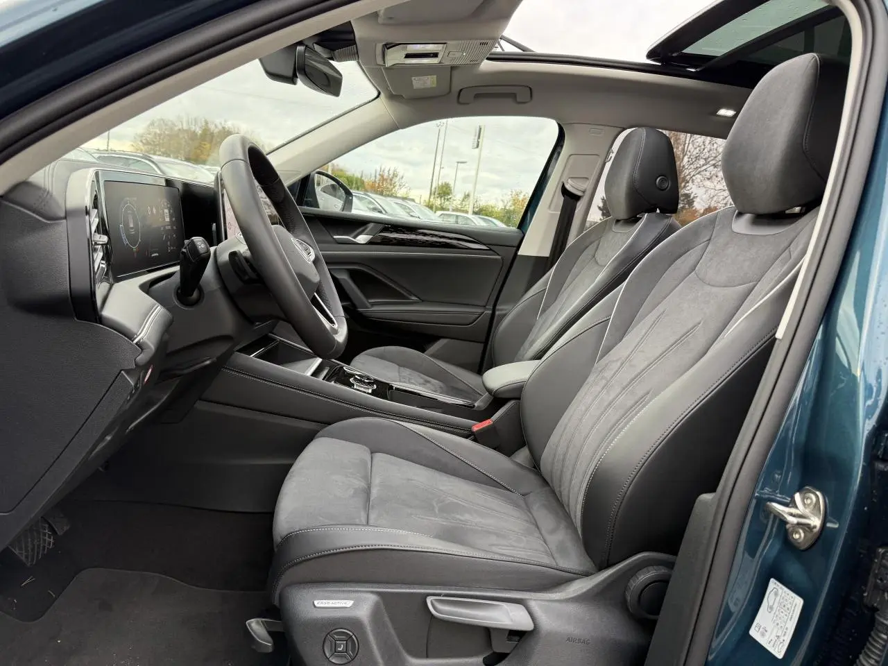 Vue intérieure côté conducteur du Volkswagen Tiguan 2024 bleu Nightshade avec sièges gris et toit ouvrant panoramique.