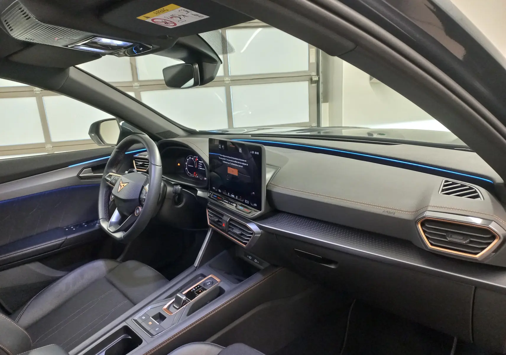 Intérieur de la CUPRA Formentor 1.5 EHybrid 2025 vu côté conducteur, avec éclairage d'ambiance bleu et écran tactile central.