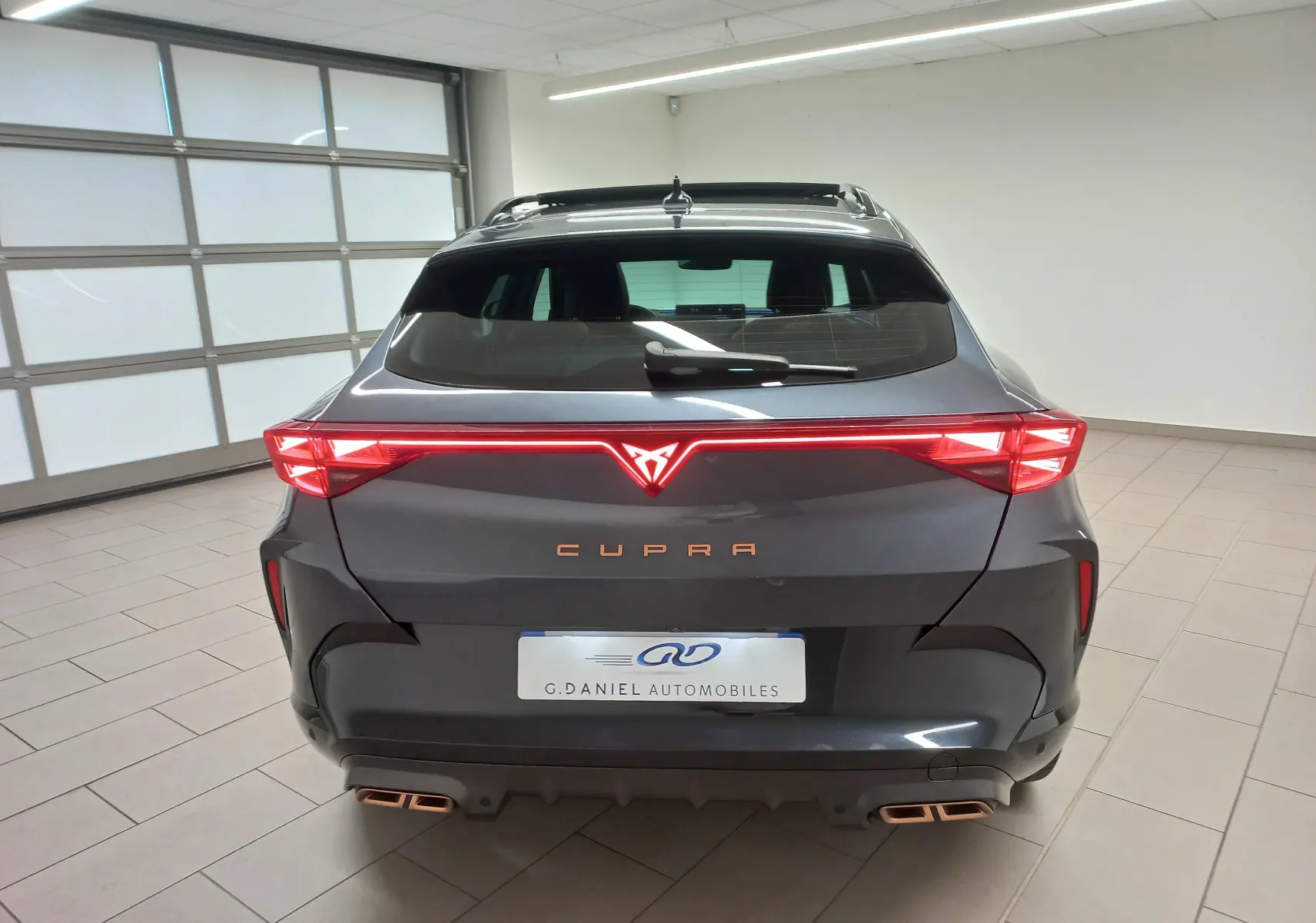 Vue arrière d'un CUPRA Formentor gris magnétique 2025 avec feux LED allumés et double sortie d'échappement cuivrée.