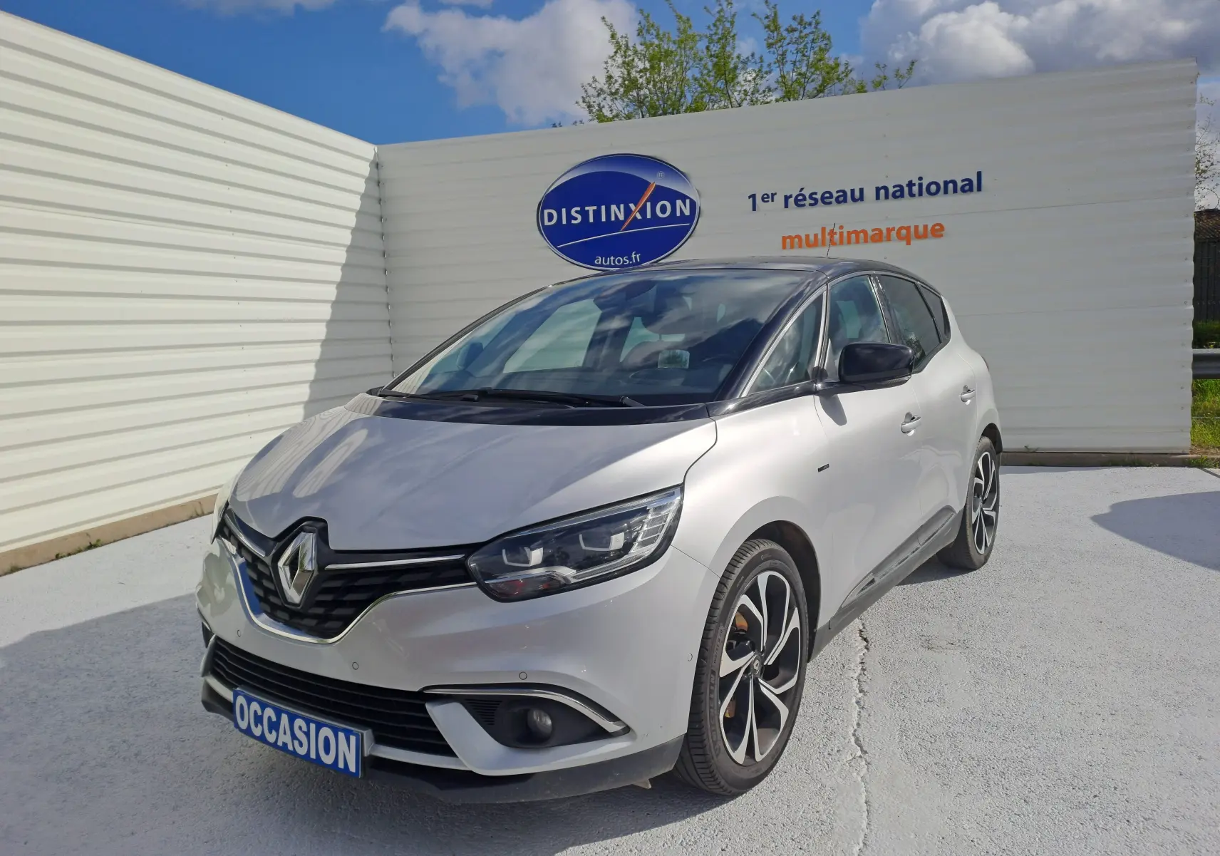 Renault Scénic IV gris platine avec toit noir, vue 3/4 avant droit, stationné devant un mur blanc.
