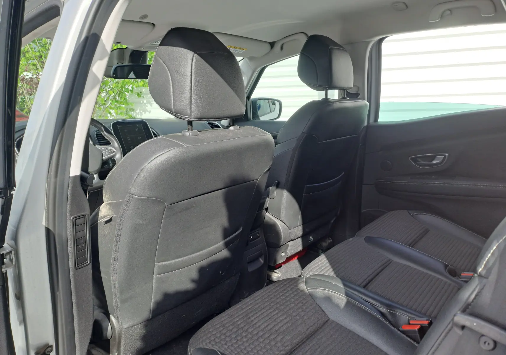 Vue intérieure arrière droite du Renault Scenic IV gris platine, sièges noirs en tissu et cuir, tableau de bord visible à l'avant.