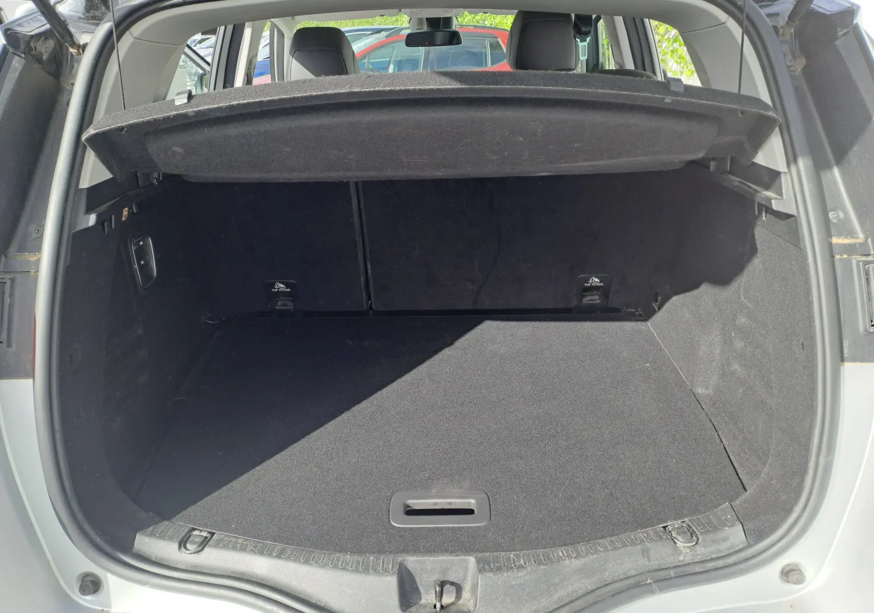 Coffre ouvert vu de l'arrière d'un Renault Scénic IV gris platine avec toit noir, montrant l'espace de chargement vide.