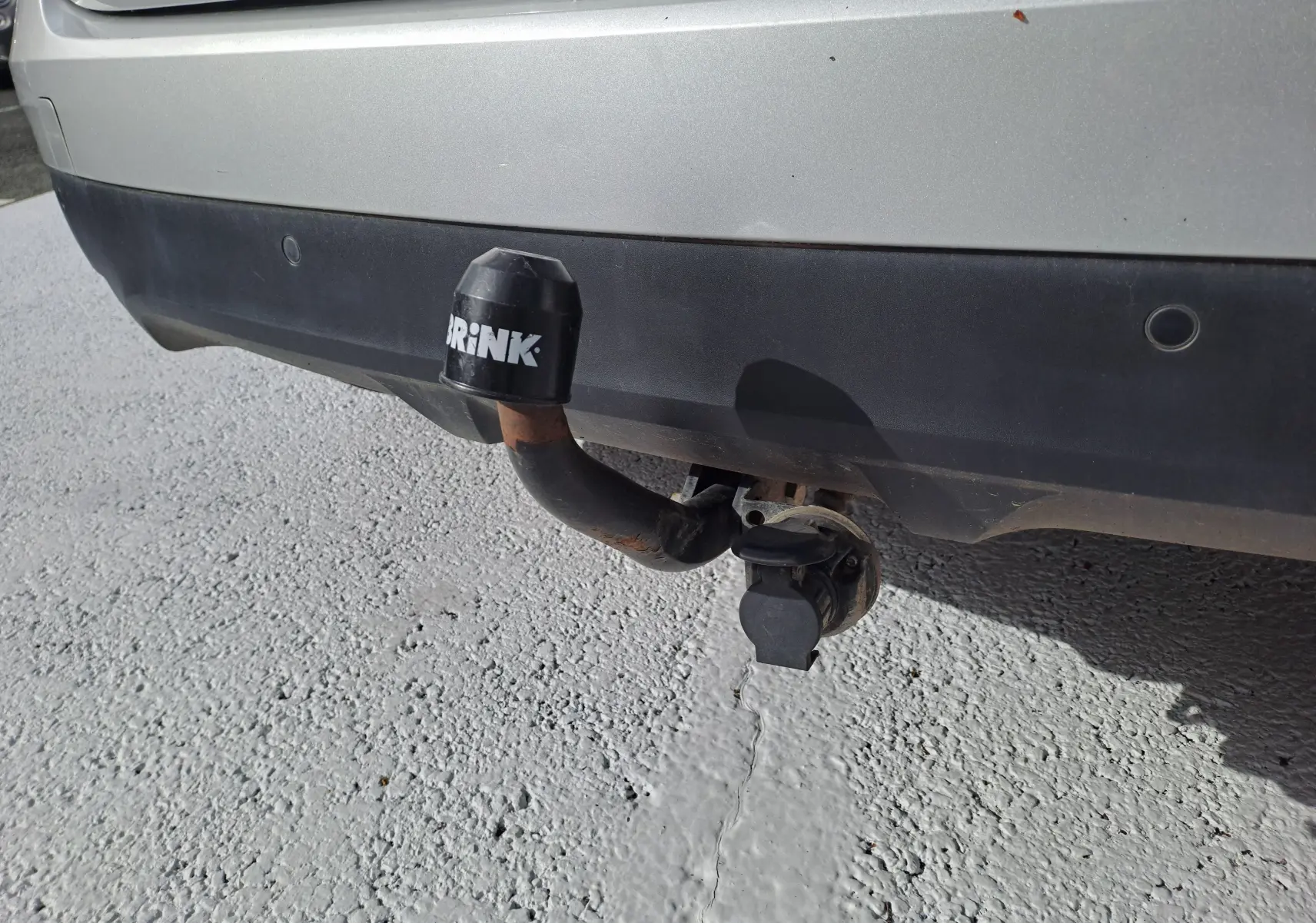 Vue rapprochée de l'attelage de remorque noir fixé au pare-chocs arrière gris platine d'un Renault Scenic IV 2018.