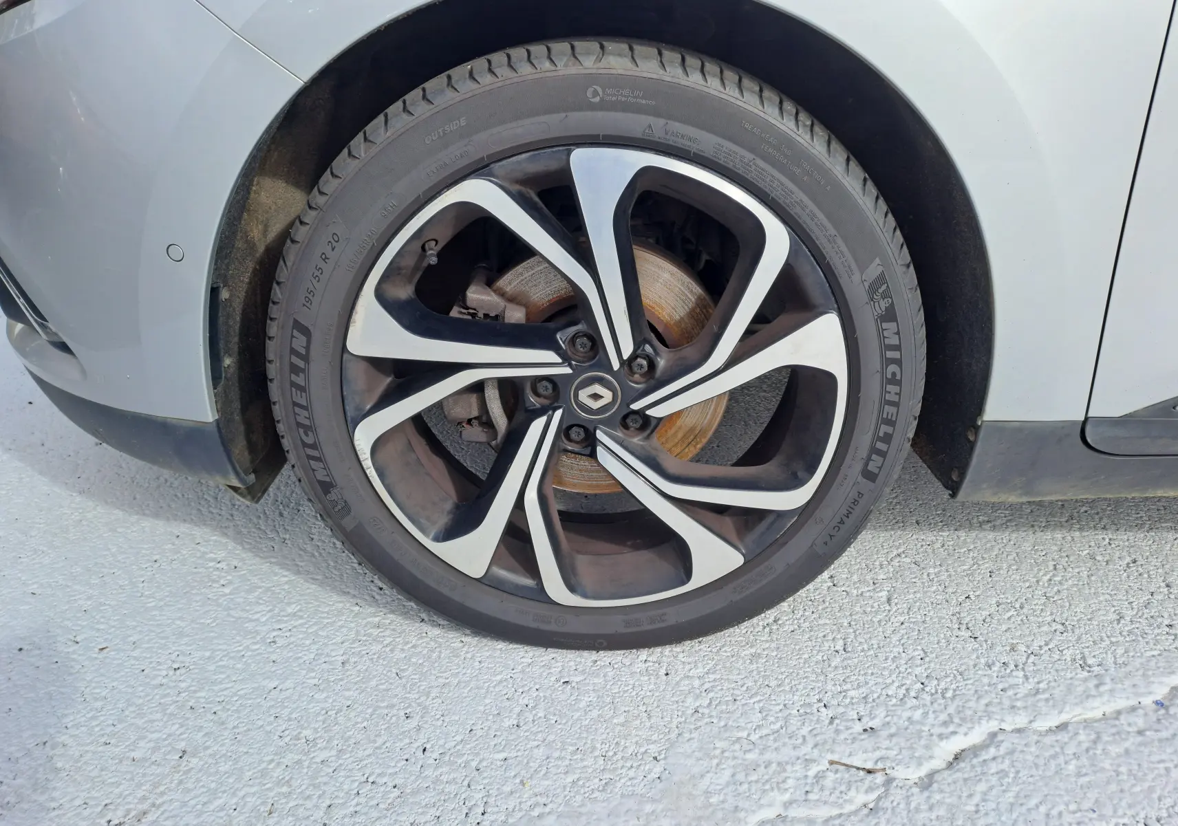 Gros plan sur la roue avant gauche du Renault Scenic IV gris platine, mettant en valeur la jante alliage noire et argentée.