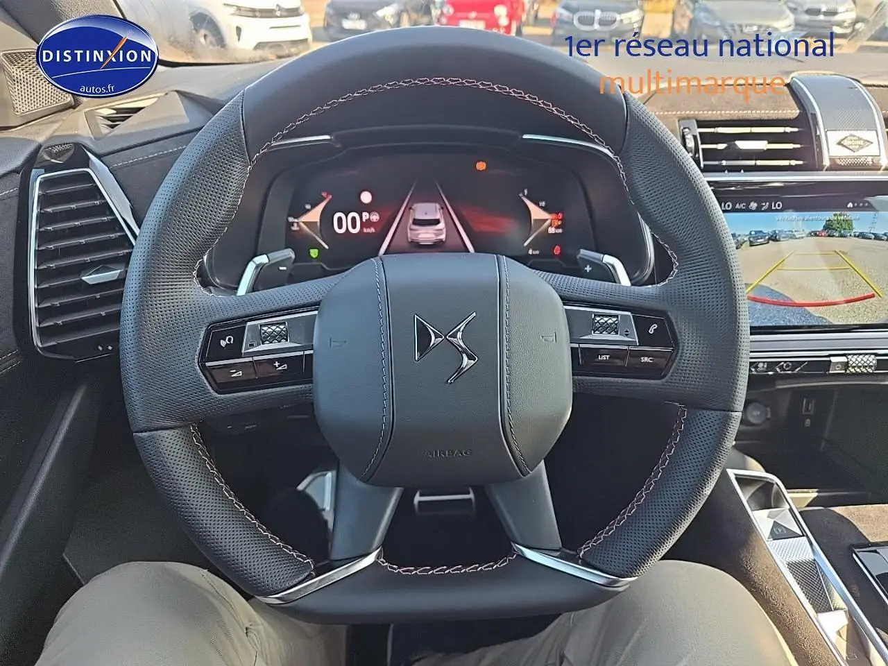 Vue intérieure centrée sur le volant DS noir avec coutures rouges et tableau de bord numérique du DS7 Cristal Pearl 2025.