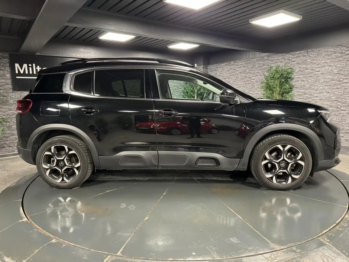 Profil côté gauche d'un SUV Citroën C5 Aircross noir nacré avec jantes alliage bi-ton dans un showroom.