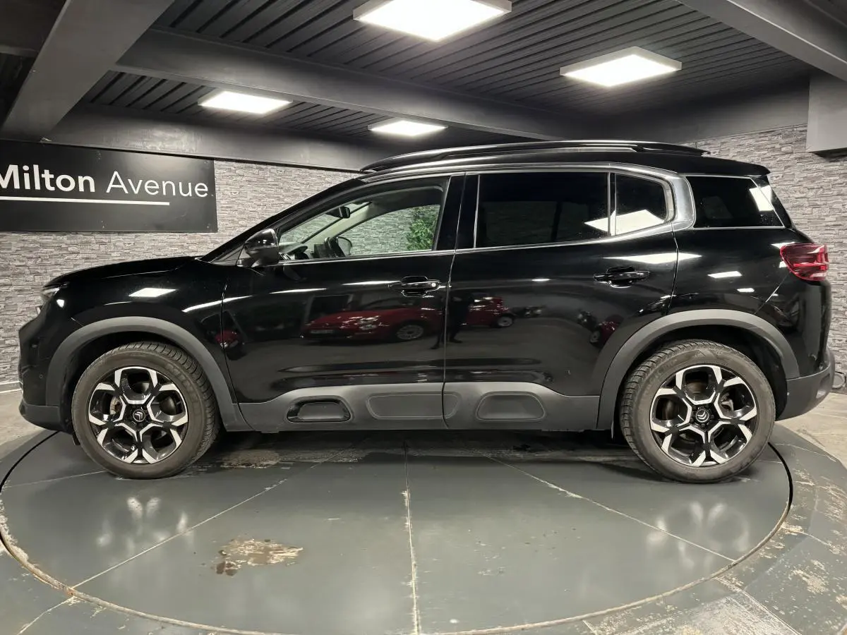 Profil latéral droit d'un Citroën C5 Aircross noir nacré avec jantes alliage bi-ton et barres de toit noires.