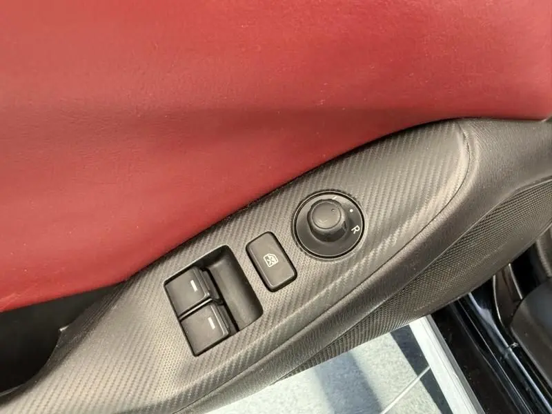 Détail de la porte côté conducteur d'une Mazda MX-5 noire 2020, avec commandes de vitres et rétroviseurs sur panneau carbone.