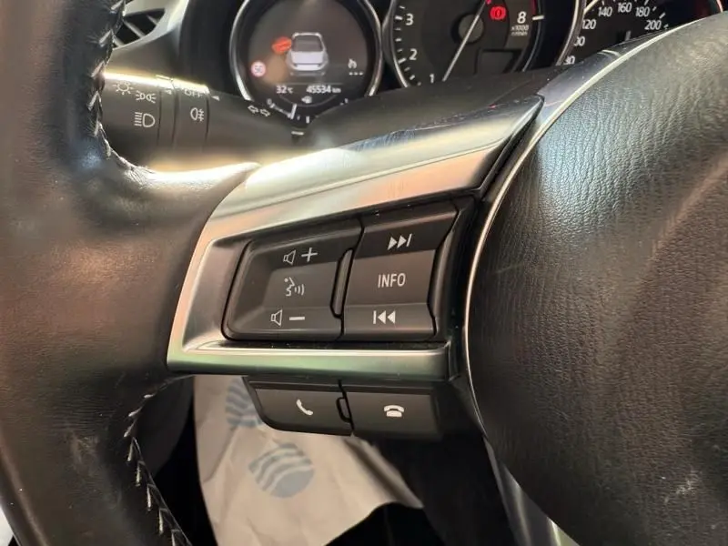 Gros plan sur les commandes au volant côté gauche d'une Mazda MX-5 noire, avec tableau de bord et compteurs en arrière-plan.