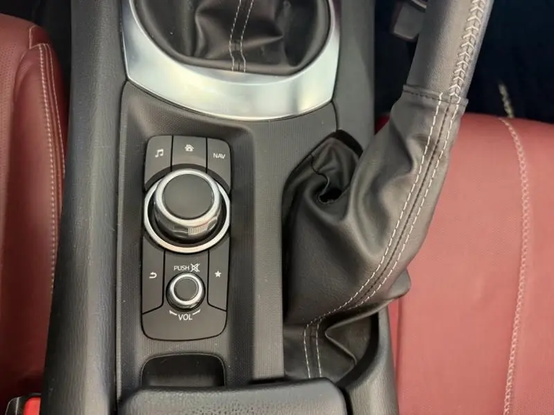 Gros plan sur la console centrale noire de la Mazda MX-5 2020, avec levier de vitesse manuel et sièges cuir rouge visibles.