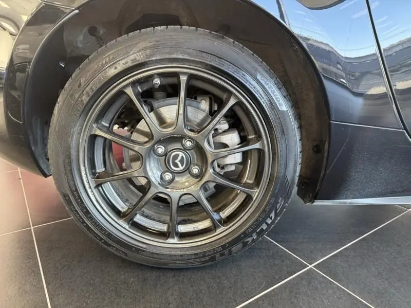 Gros plan sur la roue avant gauche noire d'une Mazda MX-5 1.5 SKYACTIV-G 2020 avec jante alliage et logo Mazda central.