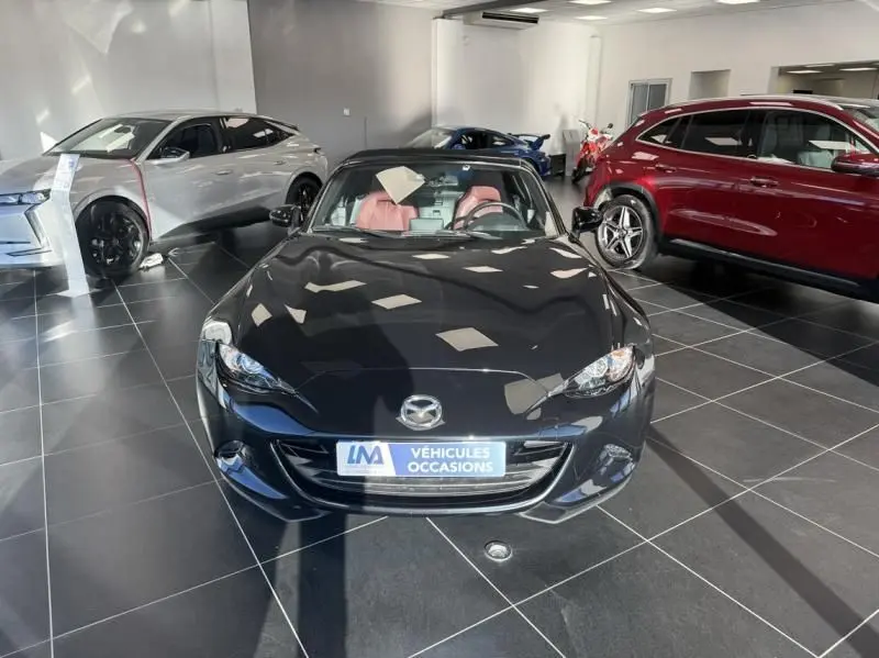Vue avant d'une Mazda MX-5 noire 2020 avec intérieur rouge, exposée dans un showroom lumineux.