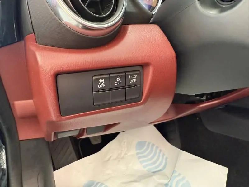 Gros plan sur les commandes de sécurité et i-stop sur le tableau de bord rouge d'une Mazda MX-5 noire, côté gauche.