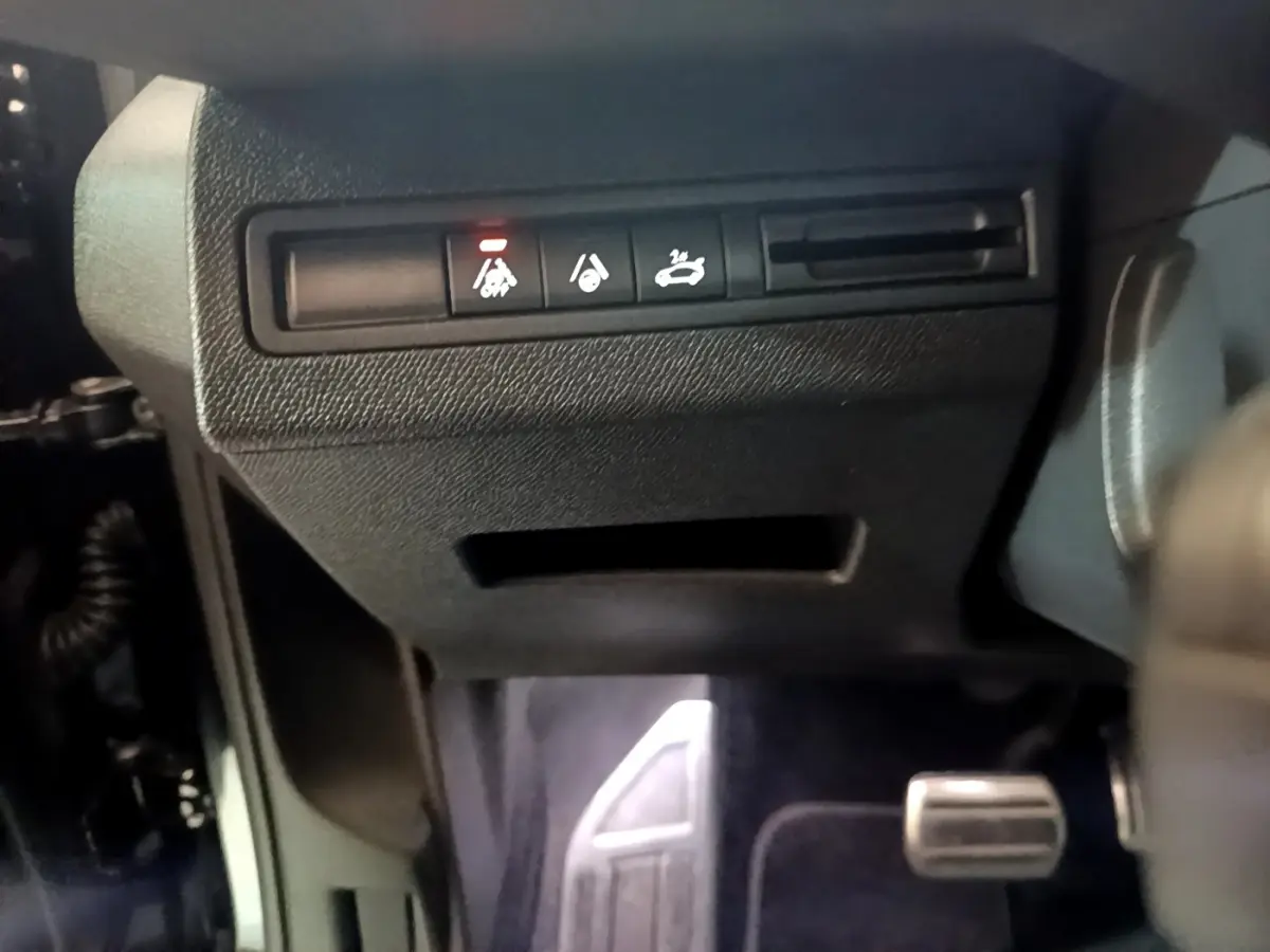 Gros plan sur les commandes sous le tableau de bord côté gauche du Peugeot 3008 noir, avec témoin lumineux rouge allumé.