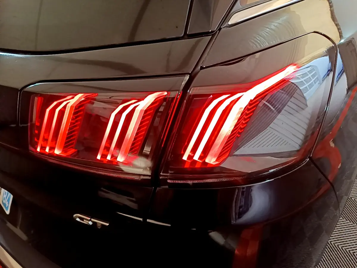 Gros plan sur le feu arrière droit rouge vif d’un Peugeot 3008 GT noir brillant de 2023.
