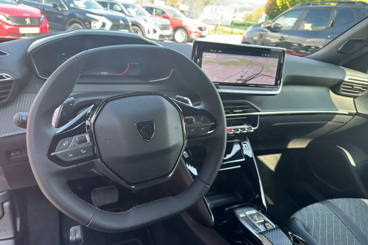 Vue intérieure centrée sur le volant cuir multifonctions et l'écran tactile 10 pouces du Peugeot 2008 Hybrid rouge Elixir.