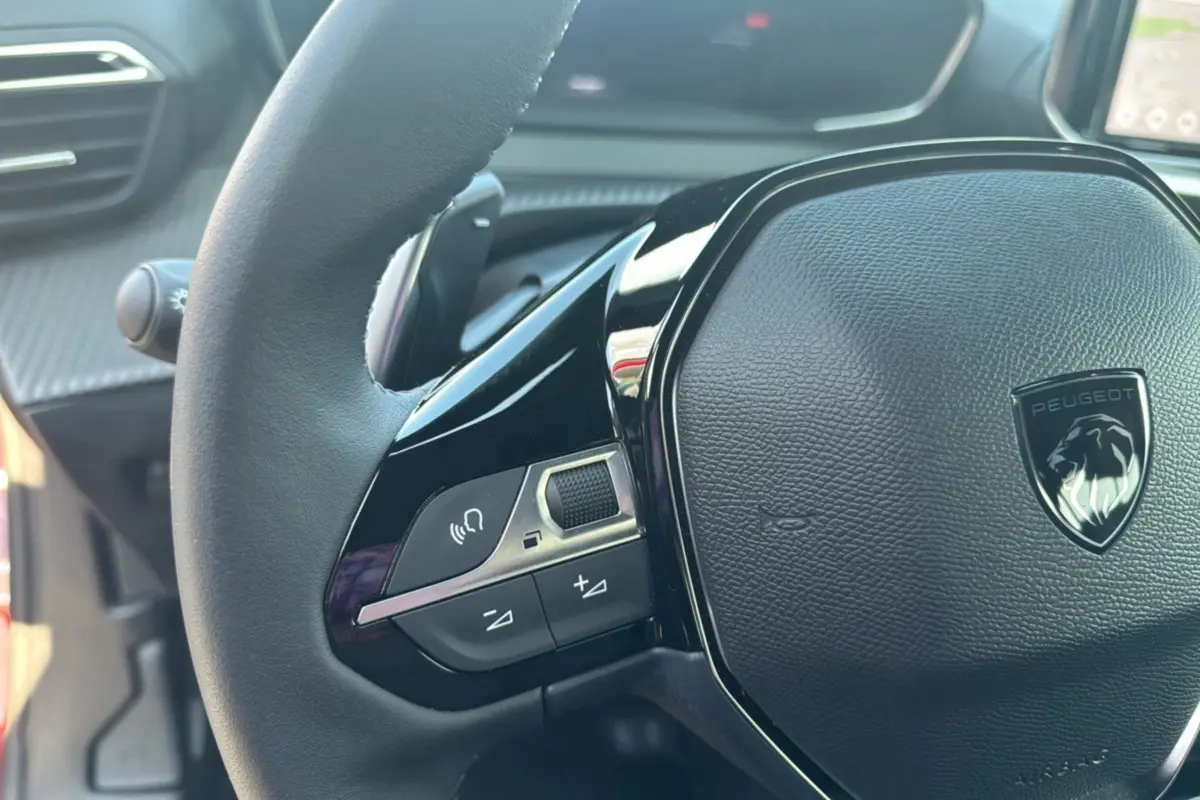 Gros plan sur le volant cuir noir multifonctions du Peugeot 2008 Hybrid 145, avec logo lion argenté au centre.