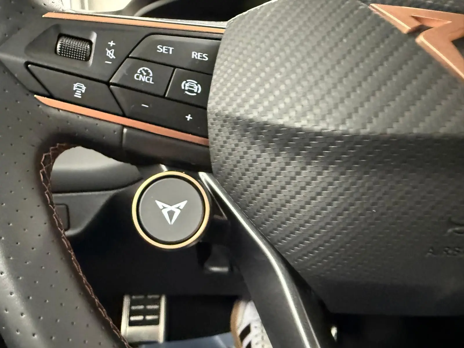 Gros plan sur le volant en carbone et cuir perforé avec logo CUPRA et commandes d'assistance au conducteur.