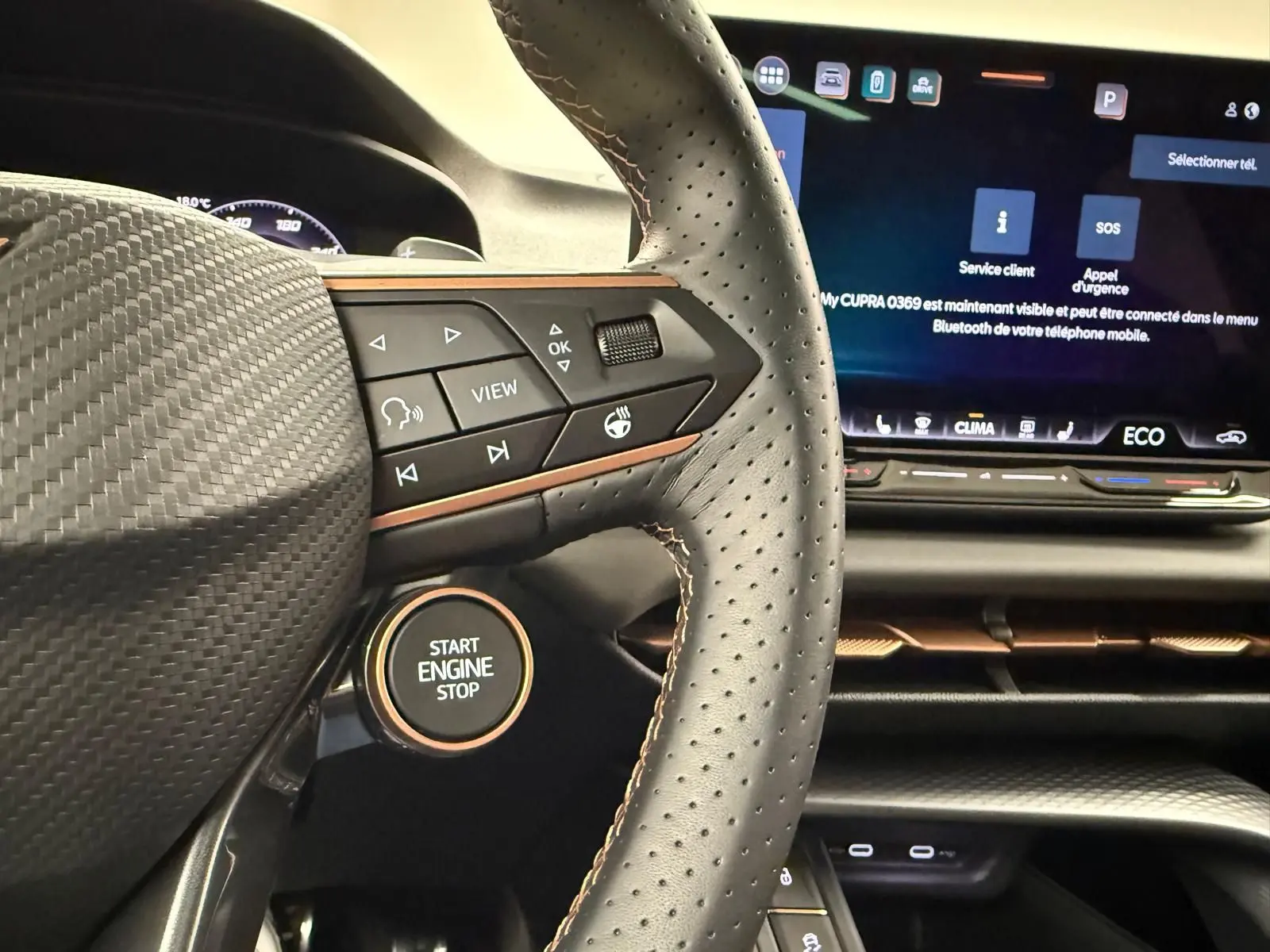 Gros plan sur le volant perforé et le bouton start/stop du CUPRA TERRAMAR 1.5 eHybrid bleu Fjord, avec écran tactile en arrière-plan.