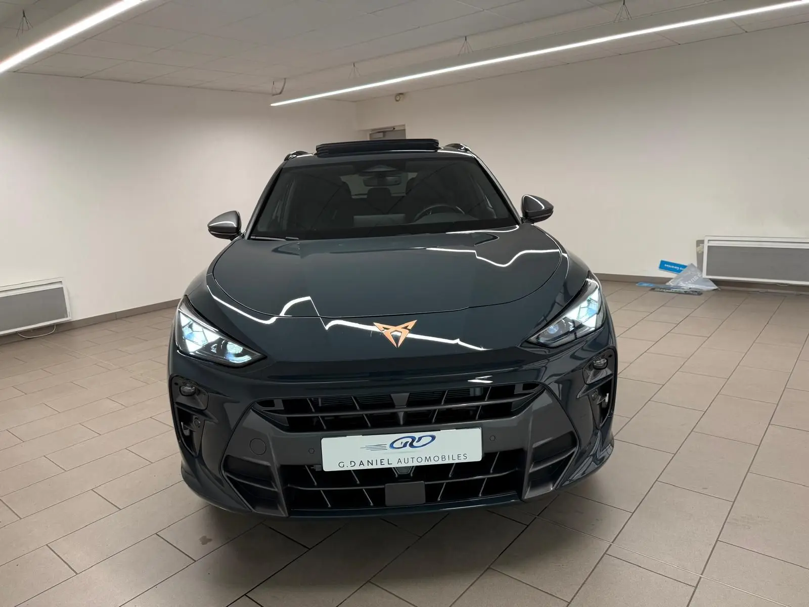 Vue avant d'une CUPRA TERRAMAR Bleu Fjord avec toit ouvrant panoramique et jantes cuivrées en intérieur showroom.