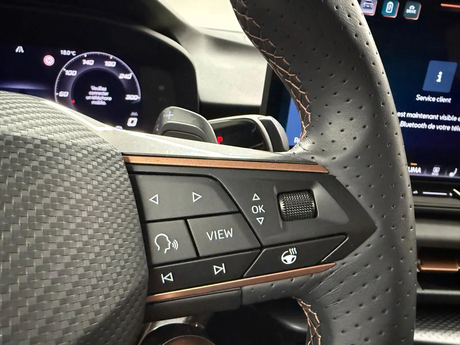 Gros plan sur les commandes du volant en cuir perforé avec surpiqûres cuivrées du CUPRA TERRAMAR hybride bleu Fjord.