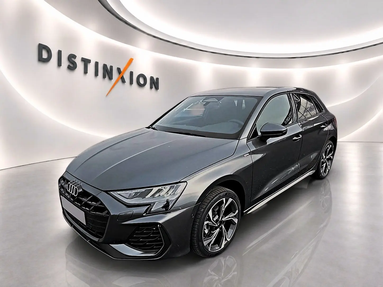 Audi A3 Sportback gris Daytona vue 3/4 avant droit en intérieur avec jantes alu et calandre noire distinctive.