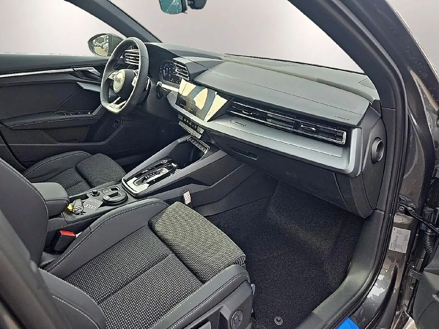 Intérieur avant droit de l'Audi A3 Sportback 2026 gris Daytona, avec tableau de bord moderne et sièges sport noirs.
