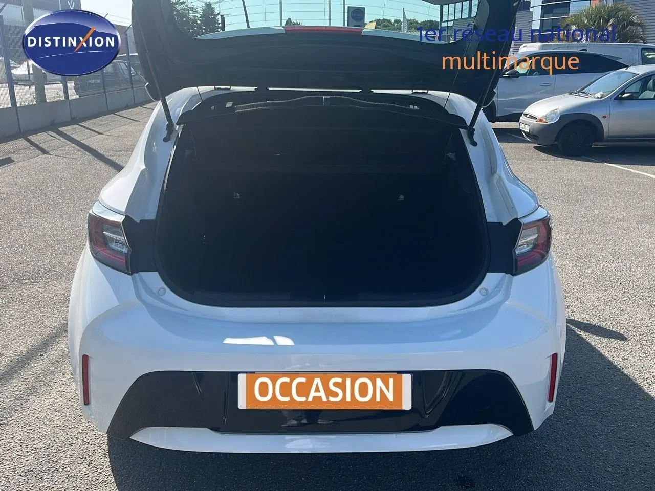 Vue arrière d'une Toyota Corolla blanche 2023 avec coffre ouvert sur un parking ensoleillé.