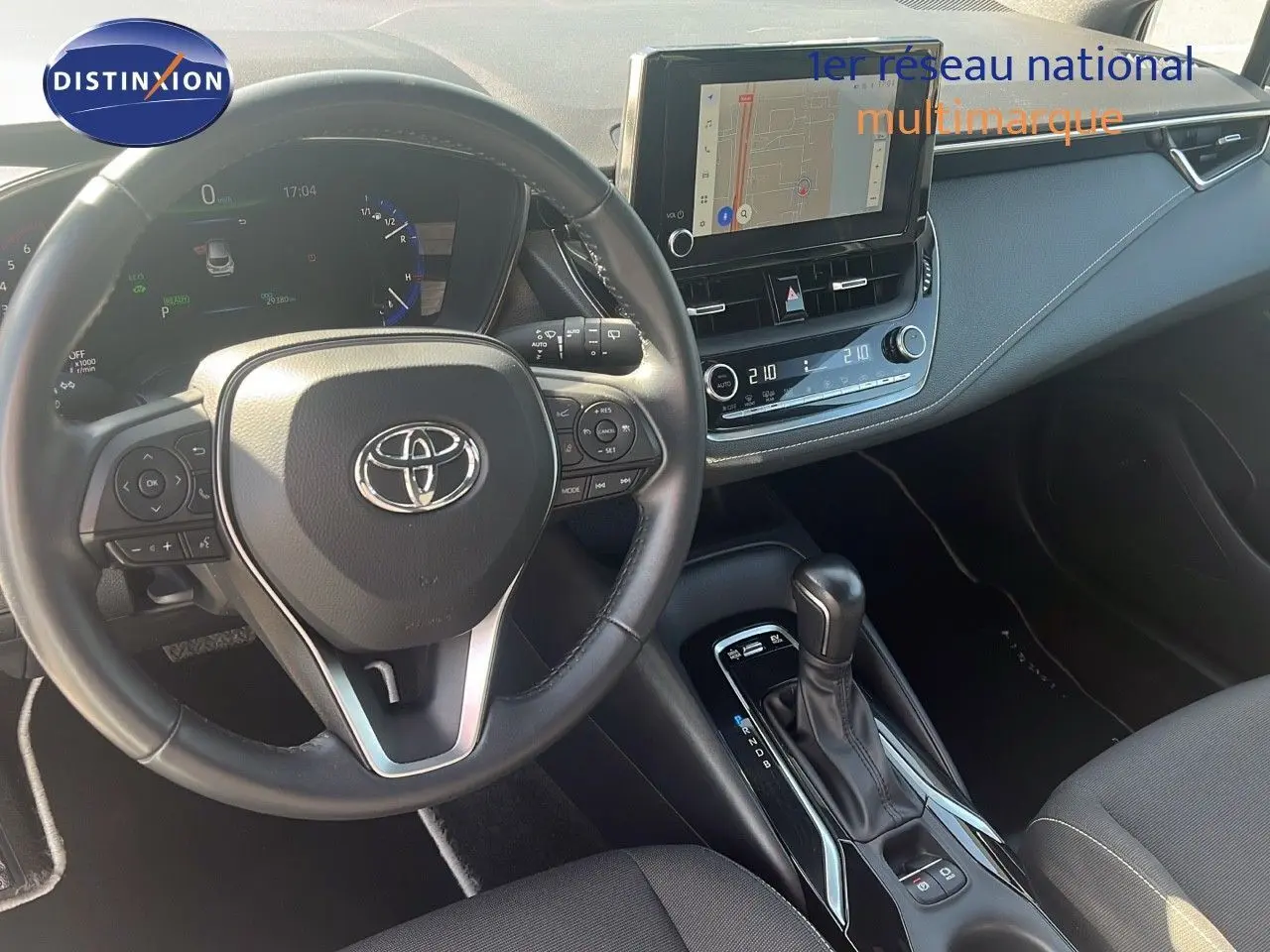 Intérieur de la Toyota Corolla 2023 hybride, vue du poste de conduite avec volant multifonction et écran tactile central.