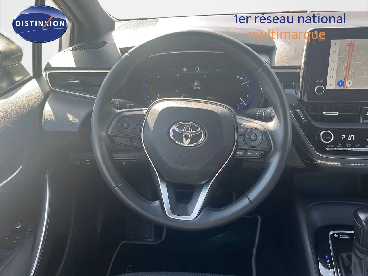 Vue intérieure centrée sur le volant Toyota d'une Corolla blanche 2023, avec tableau de bord numérique et écran tactile visible.