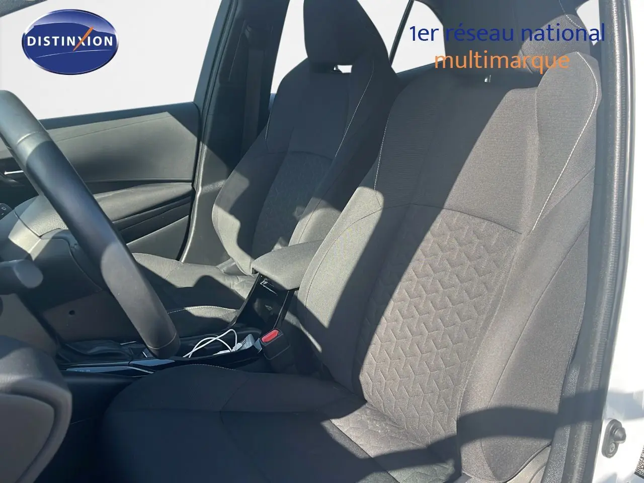 Intérieur de la Toyota Corolla 2023 blanc pur, vue côté gauche sur les sièges avant en tissu noir avec motifs géométriques.