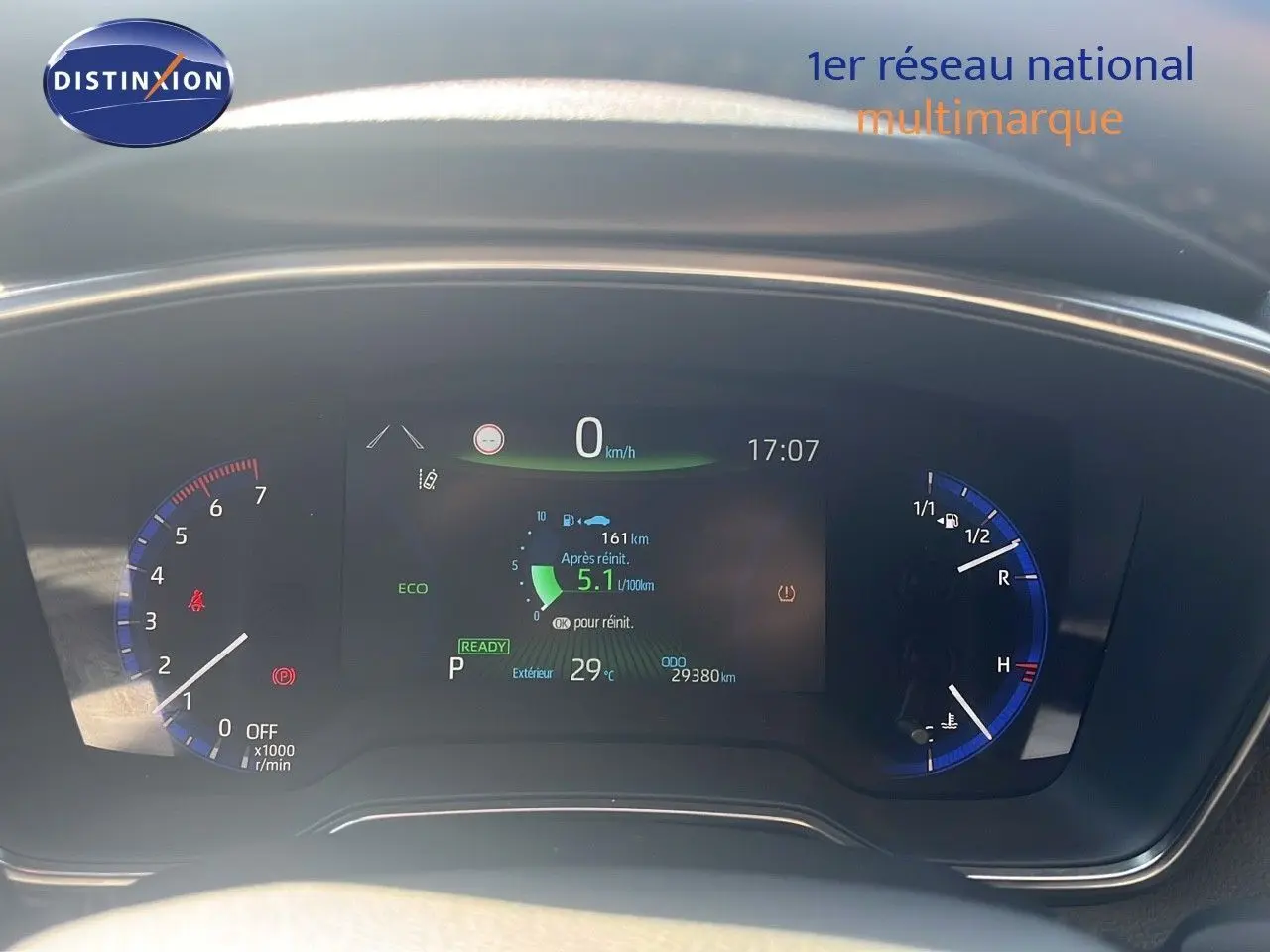 Tableau de bord numérique de la Toyota Corolla blanche 2023, affichant vitesse, consommation et température extérieure.