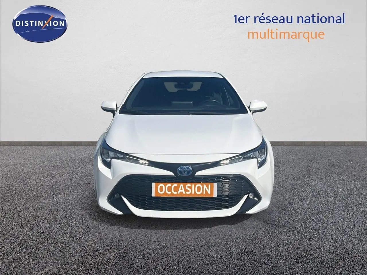 Vue frontale d'une Toyota Corolla 1.8 HSD blanche avec calandre noire et plaque "OCCASION" visible.