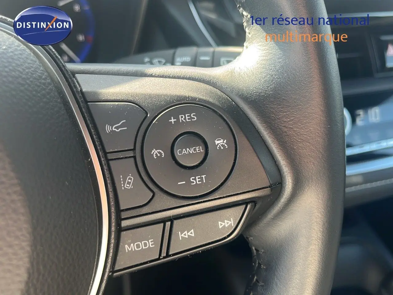 Gros plan sur les commandes au volant d'une Toyota Corolla blanche hybride 2023, mettant en valeur les boutons de régulateur de vitesse.