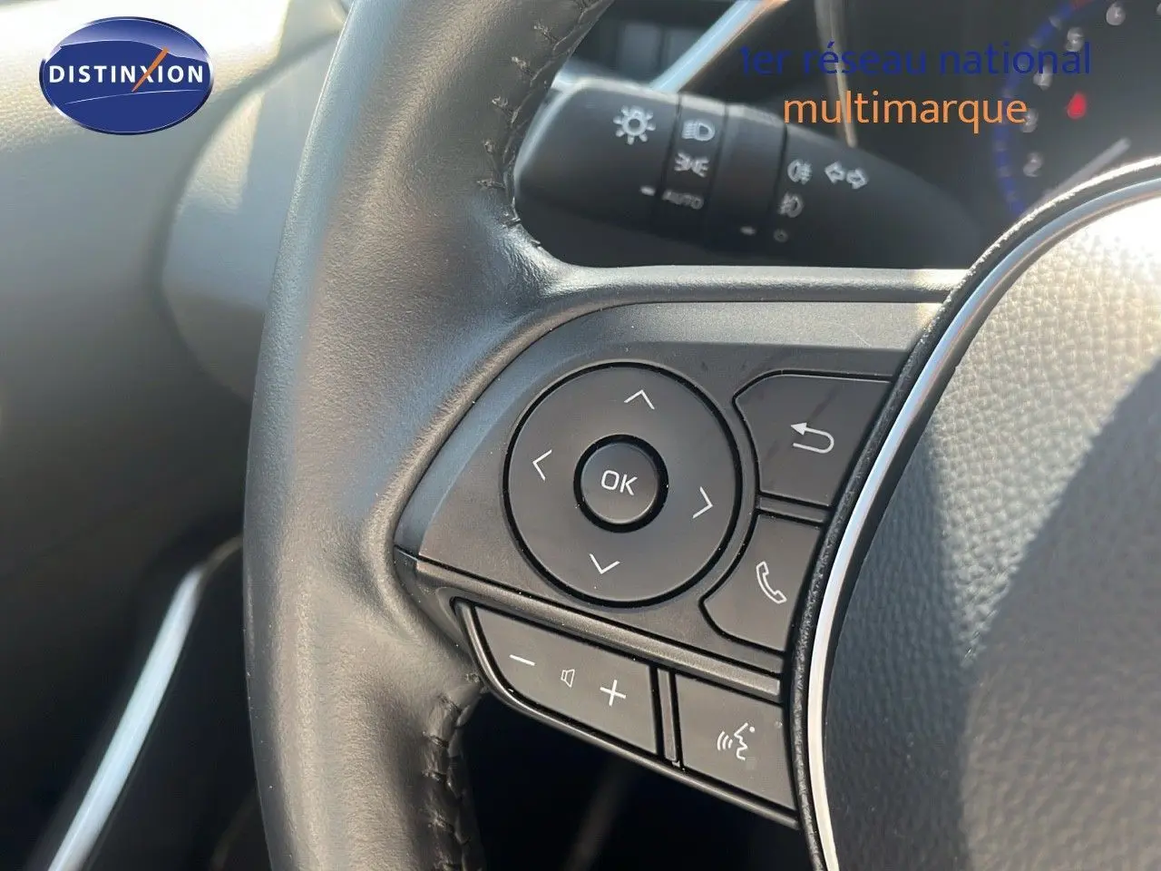 Gros plan sur les commandes au volant noir de la Toyota Corolla blanche hybride 2023, côté gauche du conducteur.