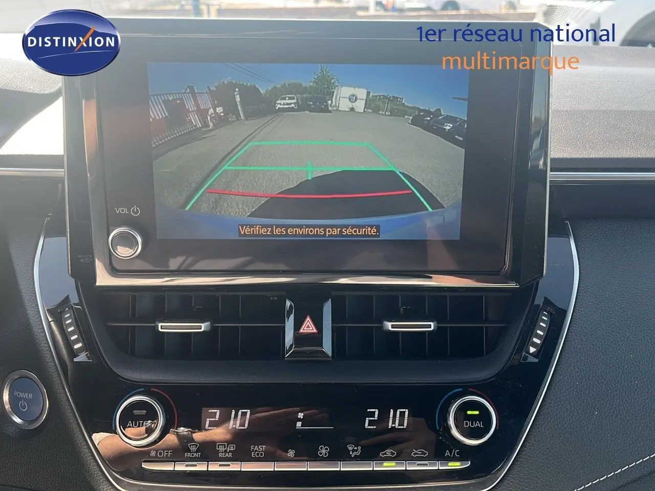 Vue rapprochée de l'écran multimédia et de la console centrale de la Toyota Corolla blanche avec caméra de recul affichée.