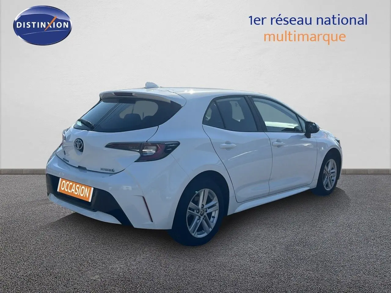 Toyota Corolla hybride blanche vue en 3/4 arrière côté droit, avec hayon et feux arrière modernes visibles.