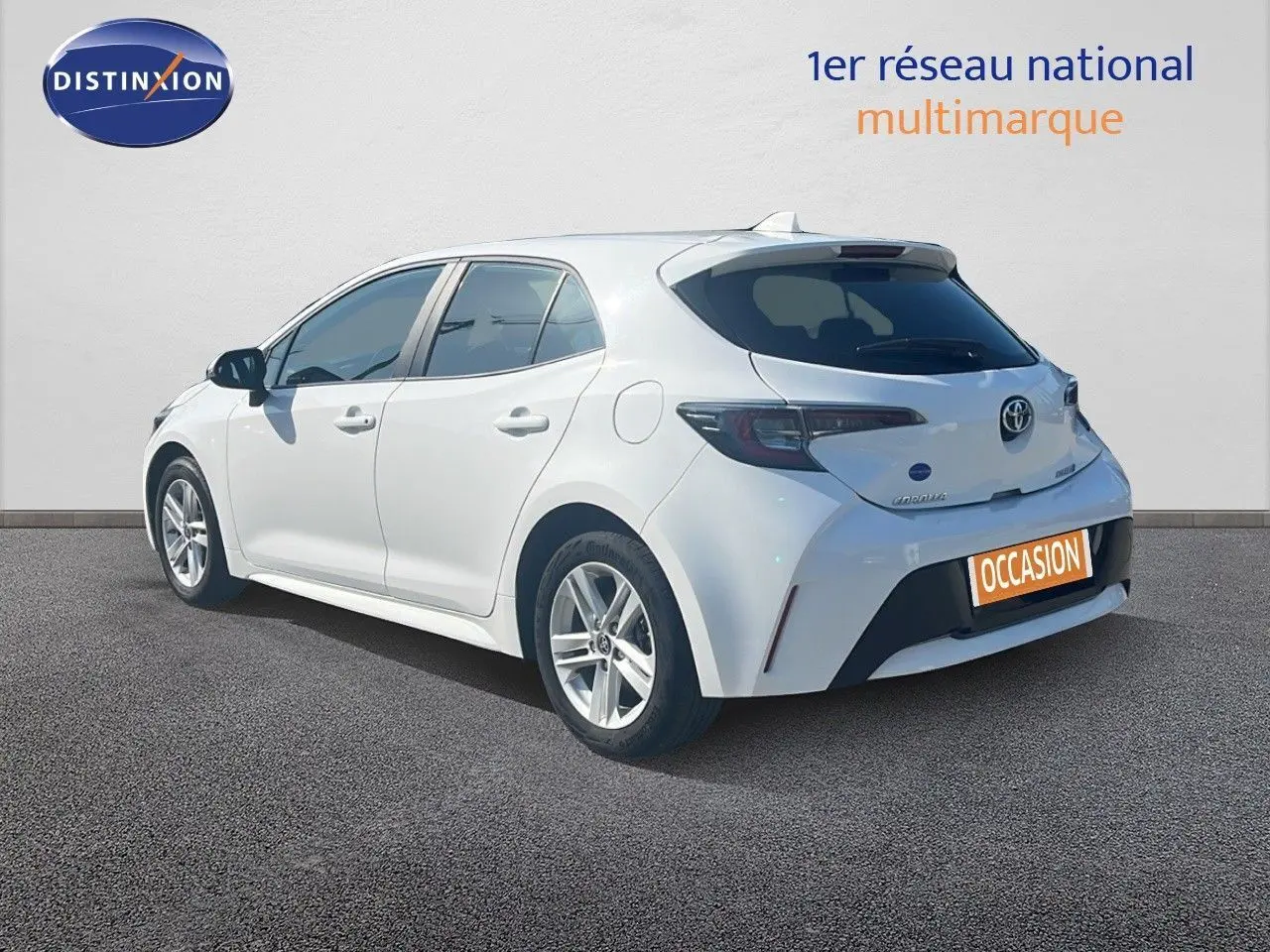 Toyota Corolla 2023 blanc pur vue 3/4 arrière côté gauche sur fond neutre avec plaque occasion orange.