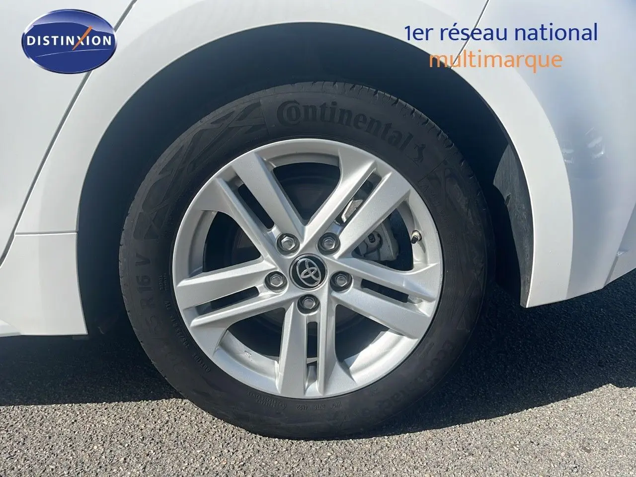 Gros plan sur la roue avant gauche blanche d'une Toyota Corolla 1.8 HSD 122CH CVT Dynamic 2023 avec jante alliage argentée.