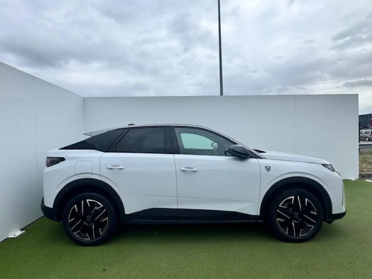 Profil côté gauche du Peugeot 3008 blanc nacré avec toit noir et jantes alliage 19 pouces diamantées sur fond extérieur neutre.