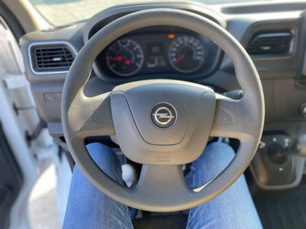 Vue rapprochée du volant noir de l'Opel Movano Fourgon blanc, avec tableau de bord et commandes visibles en arrière-plan.